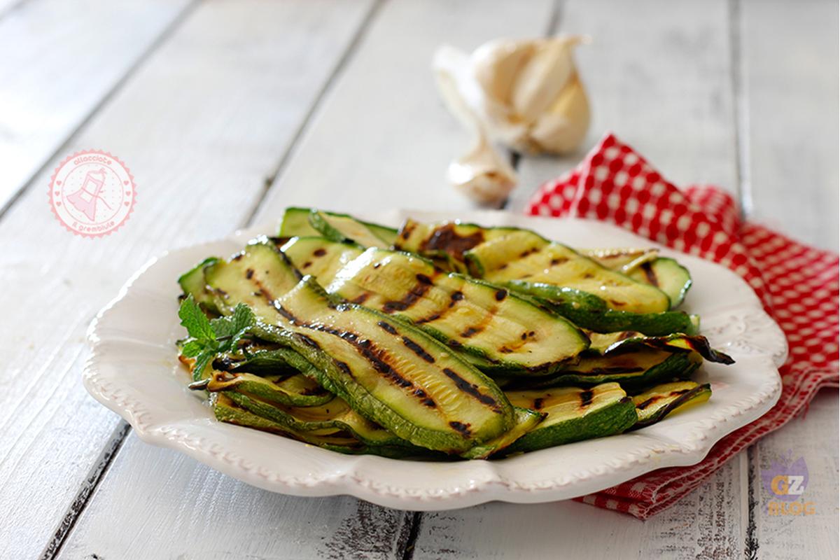 Fette di zucchine grigliate, dorate e succulente, su un piatto con erbe aromatiche fresche.